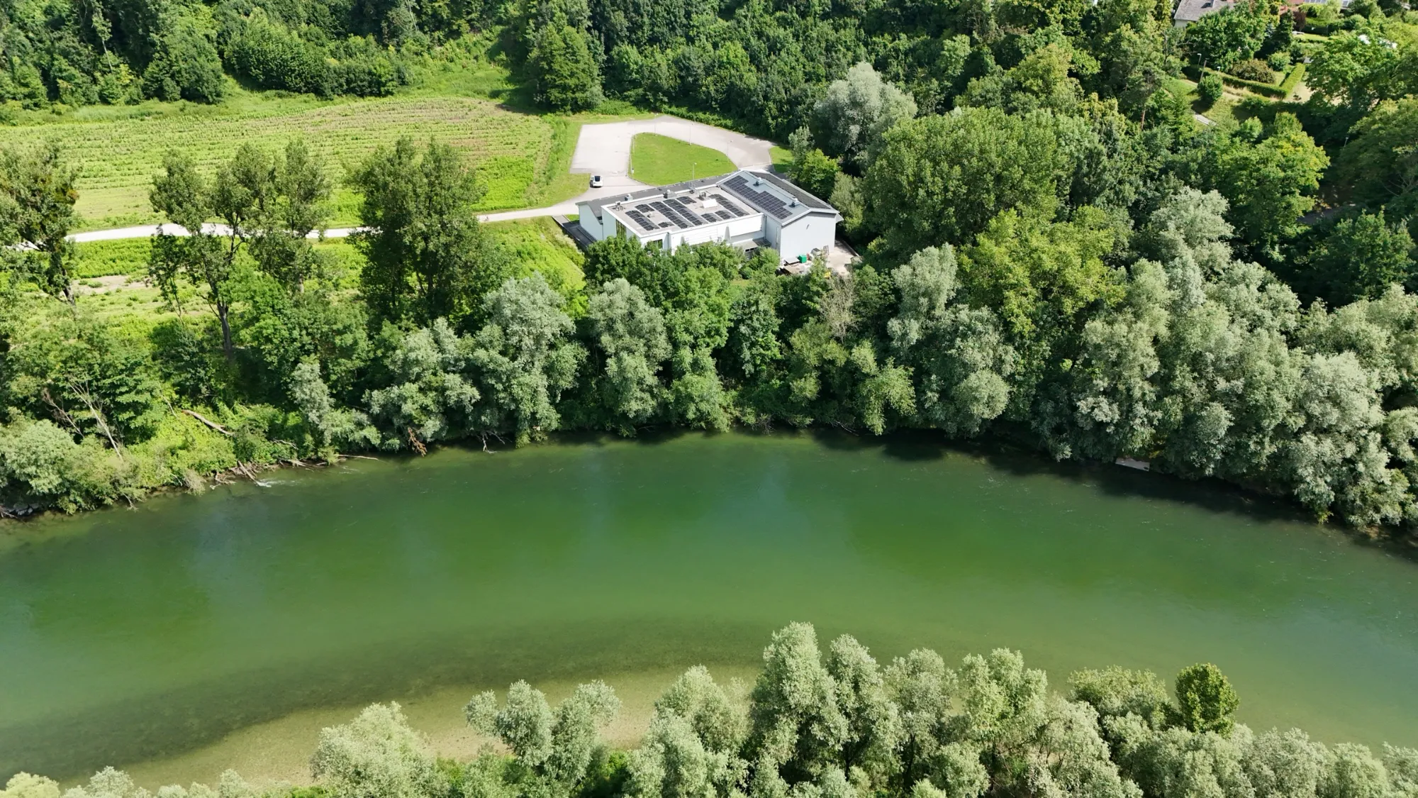 Luftaufnahme des Standorts Hofau 7 in Lambach, umgeben von Wiesen und Bäumen am Fluss